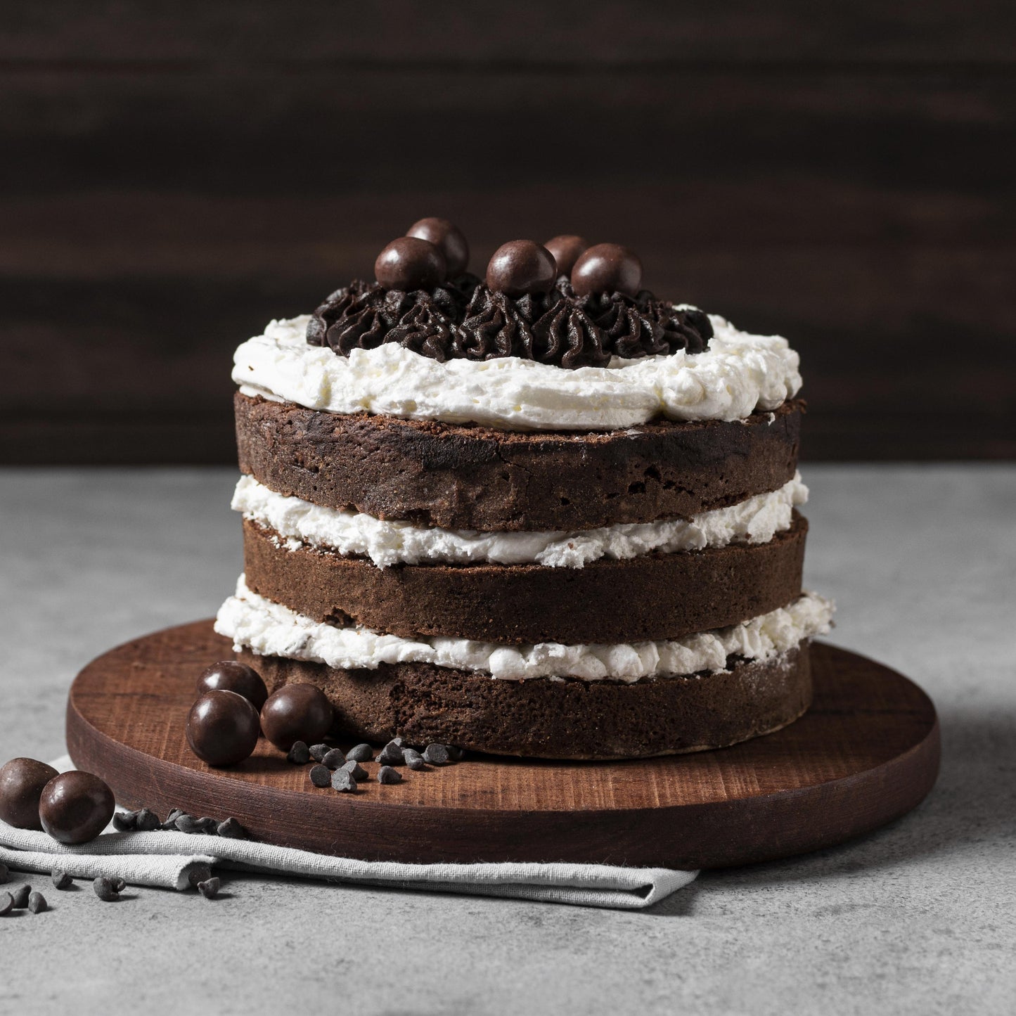 Front view of a moist chocolate cake on a round wood board, layered with cream cheese frosting, decorated with cocoa buttercream dollops, and topped with milk chocolate-covered coffee beans.