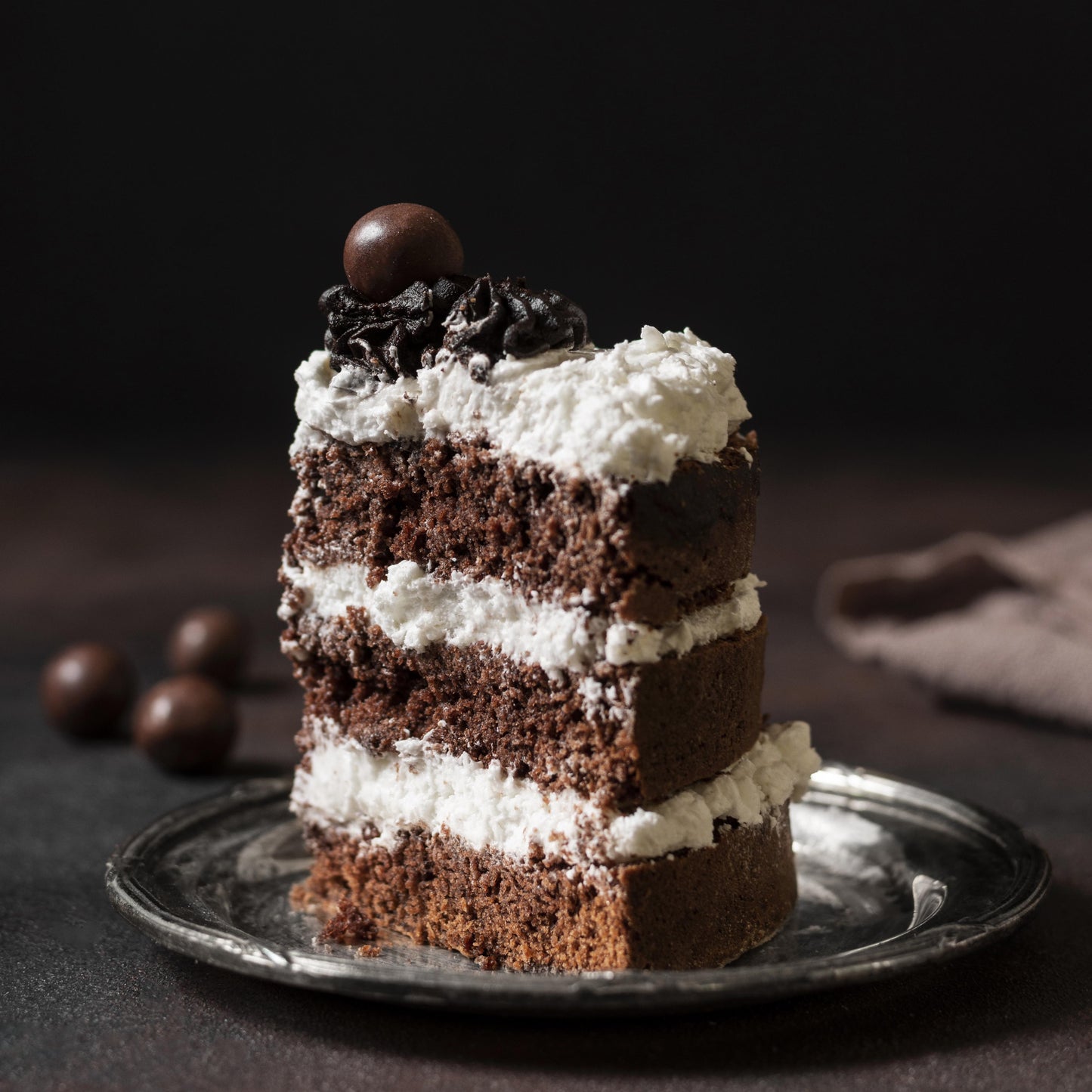 Front view of a moist chocolate cake slice on a porcelain plate, layered with cream cheese frosting, decorated with cocoa buttercream dollops, and topped with milk chocolate-covered coffee beans.