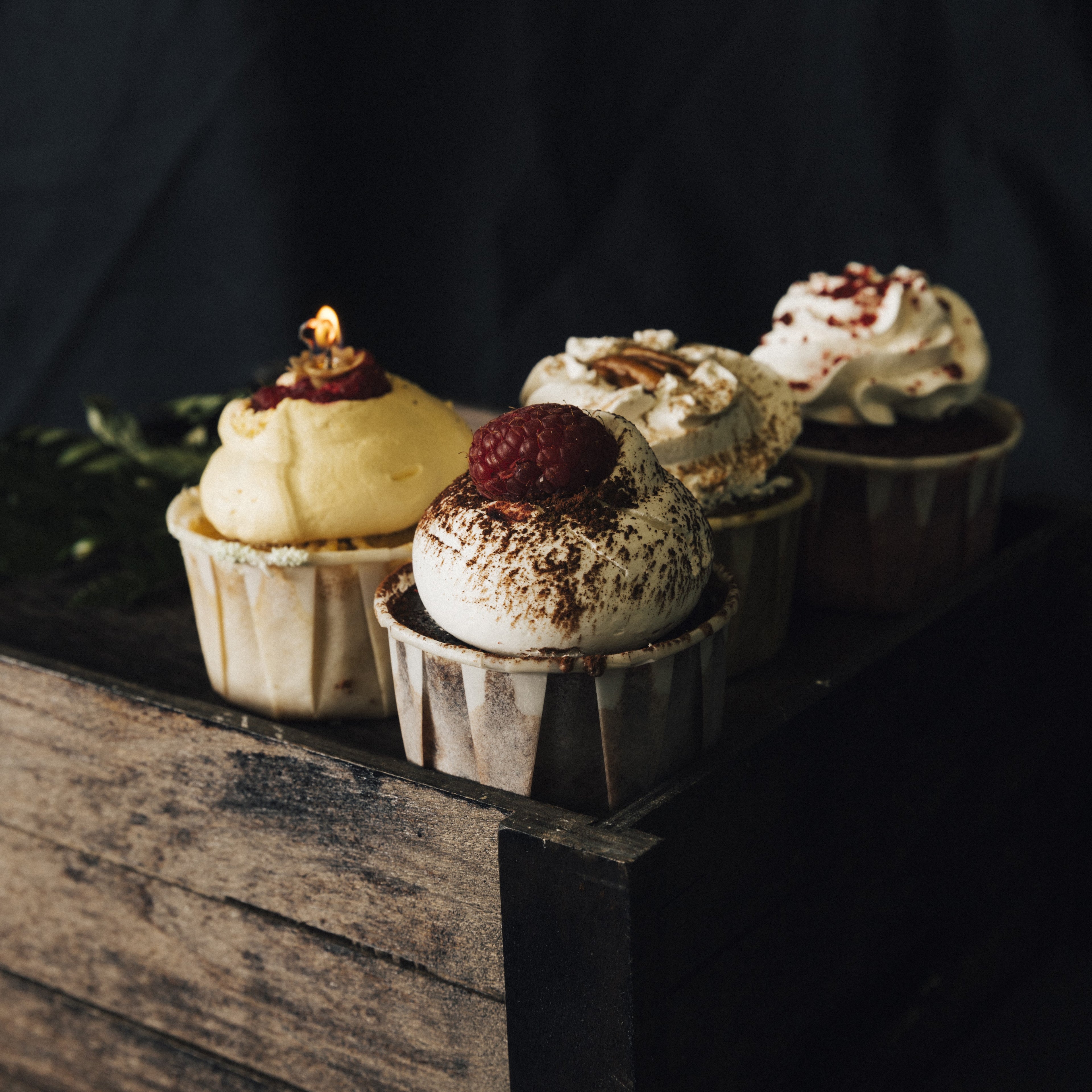 Angled front view of 4 cupcakes with buttercream, fruits, and cocoa powder on a wooden crate.