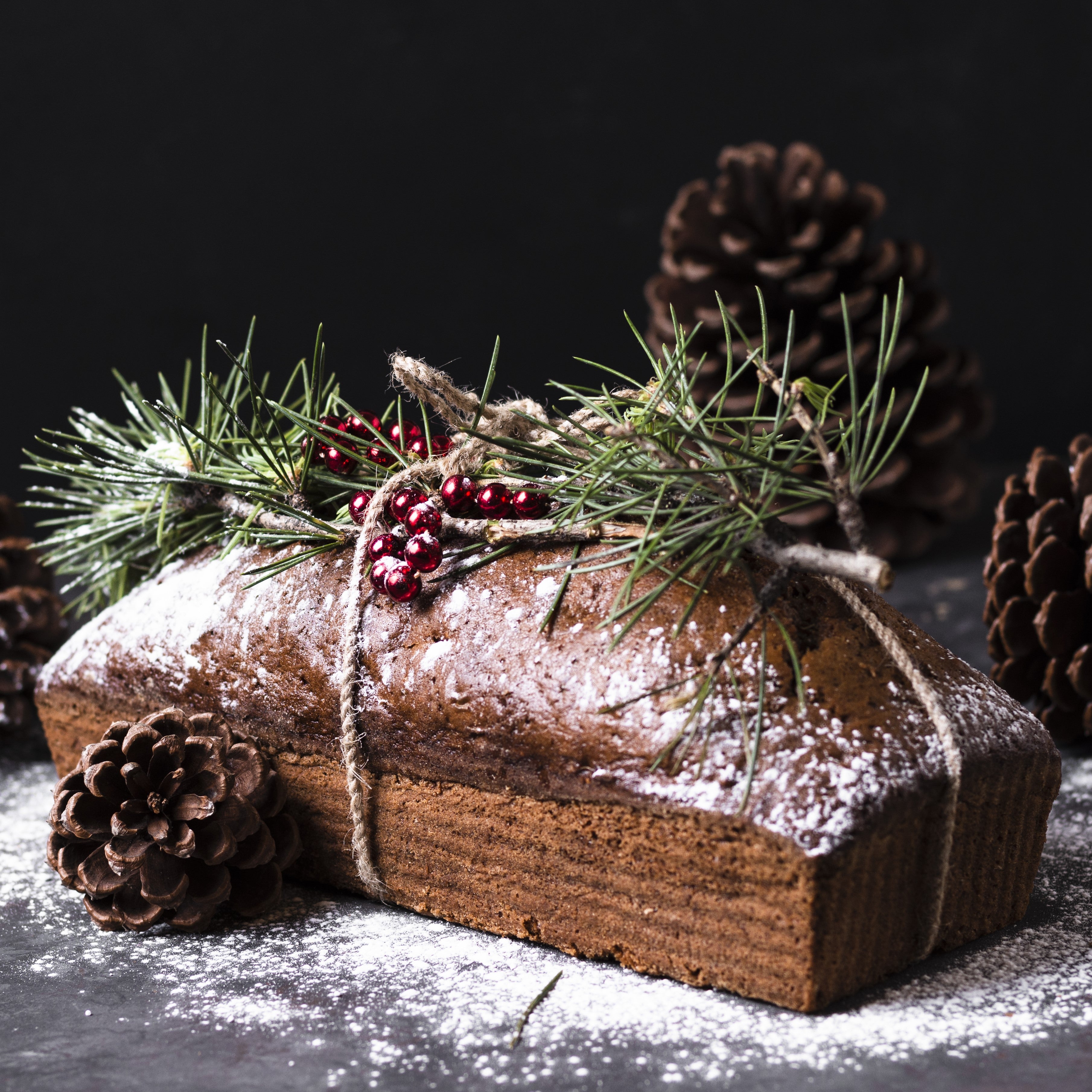 Angled front view of a Christmas-themed loaf with pine branches and pine cones on top and around it.