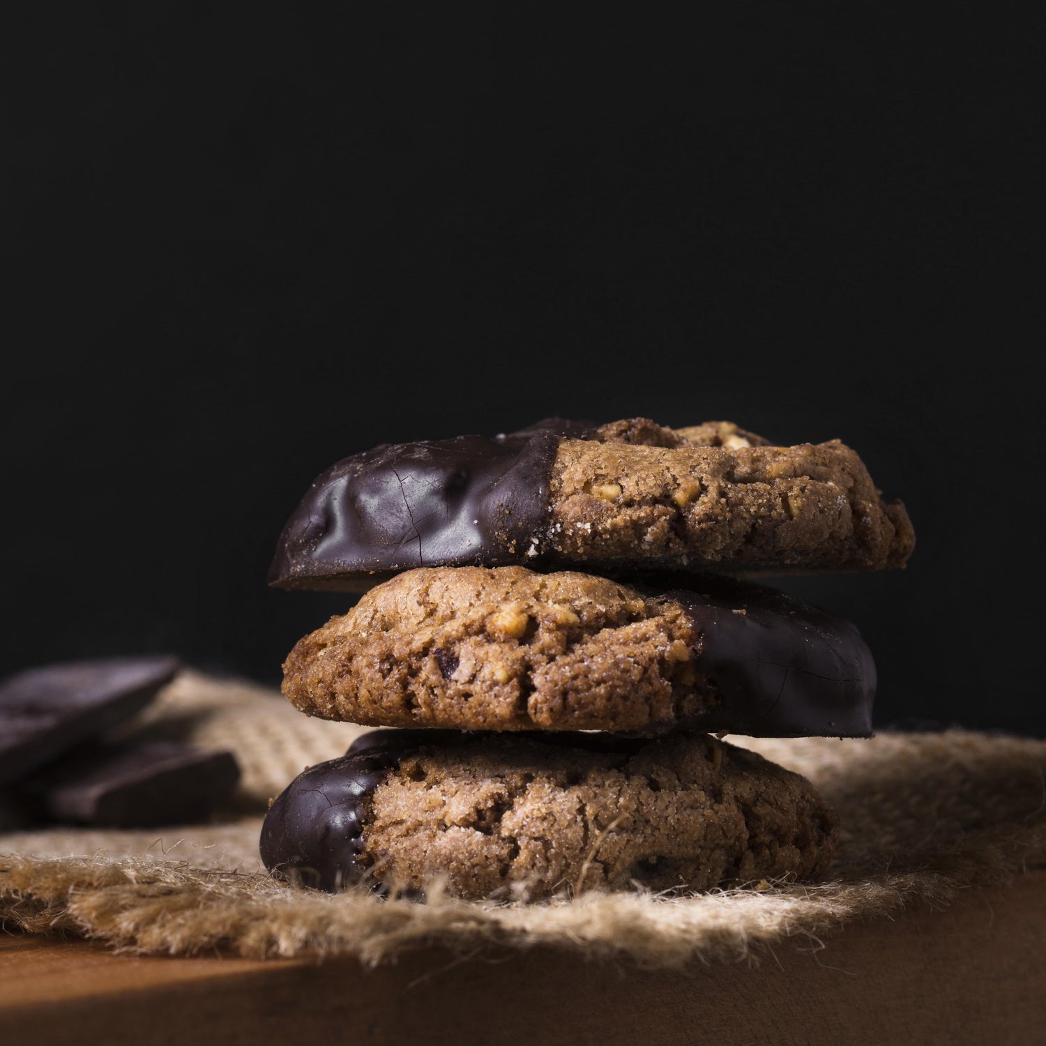 Front view of a stack of several chocolate-dipped double chocolate chip cookies on a light cloth.