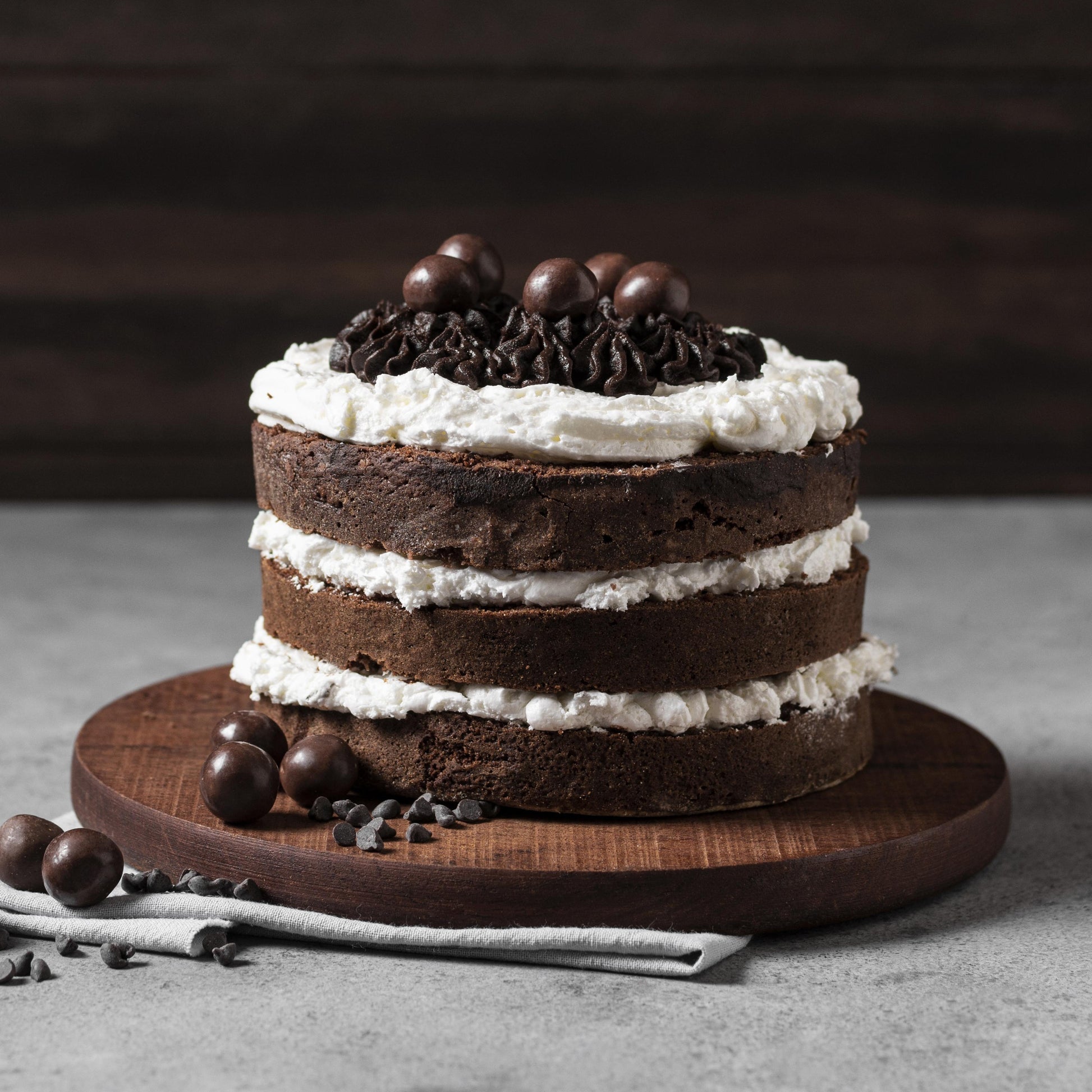 Front view of a moist chocolate cake on a round wood board, layered with cream cheese frosting, decorated with cocoa buttercream dollops, and topped with milk chocolate-covered coffee beans.