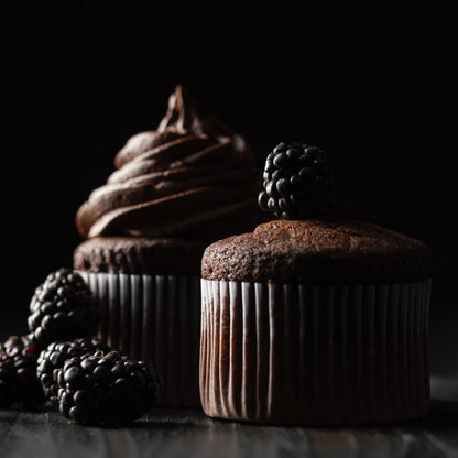 Front close-up view of two tall chocolate ramekin-shaped cupcakes, one decorated with chocolate buttercream and the other topped with fresh blackberries.