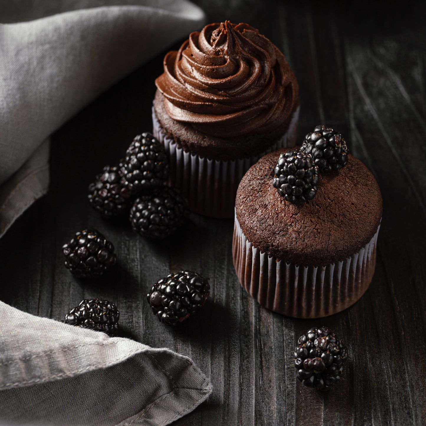 Angled top view of three tall chocolate ramekin-shaped cupcakes, two decorated with chocolate buttercream, and one topped with fresh blackberries.